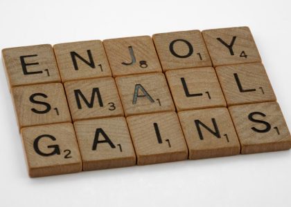 Close-up of Scrabble tiles spelling 'Enjoy Small Gains' on a white surface.